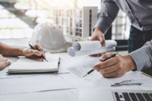 A man’s hand holding a pen going over blueprints for a design assist construction project in Meridian.